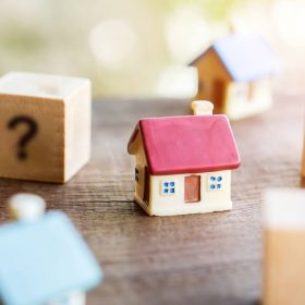 Small wooden house surrounded by question mark blocks, symbolizing important questions to ask a realtor when selling.