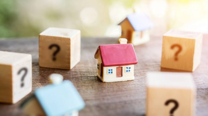 Small wooden house surrounded by question mark blocks, symbolizing important questions to ask a realtor when selling.