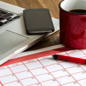 Homeowner researching the best time to sell a house with a calendar, pen, and laptop on a desk.