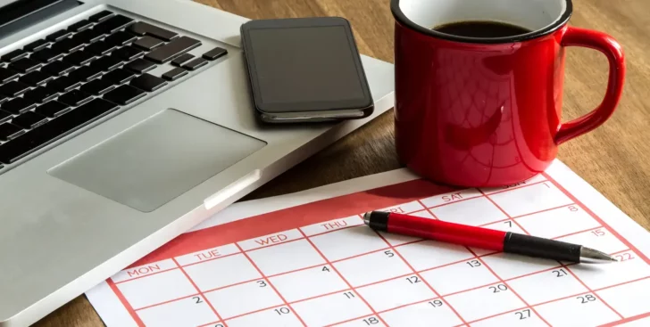 Calendar on a desk with a laptop, phone, coffee mug, and pen