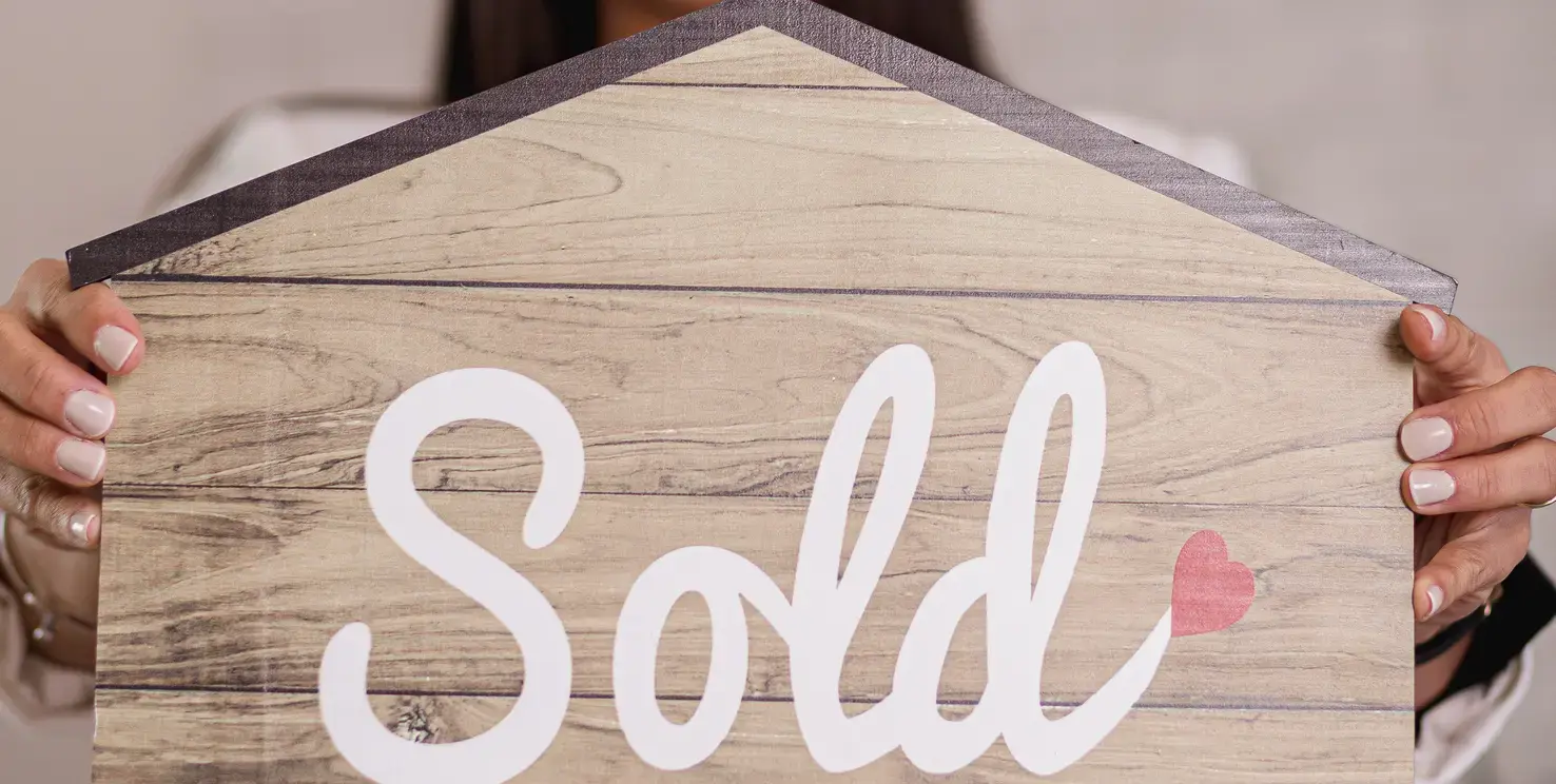 Person holding a wooden house sign that says sold