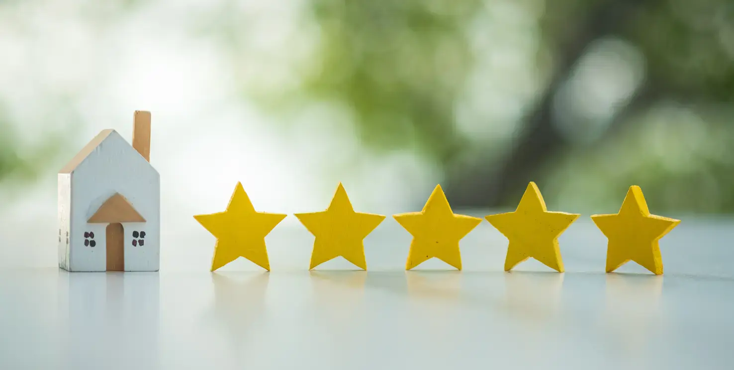 Small house model next to five stars, representing what makes a good real estate agent