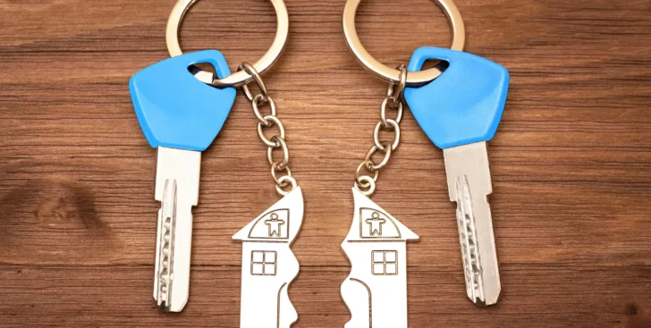 Two house keychains split apart beside two keys, representing selling a house during a divorce