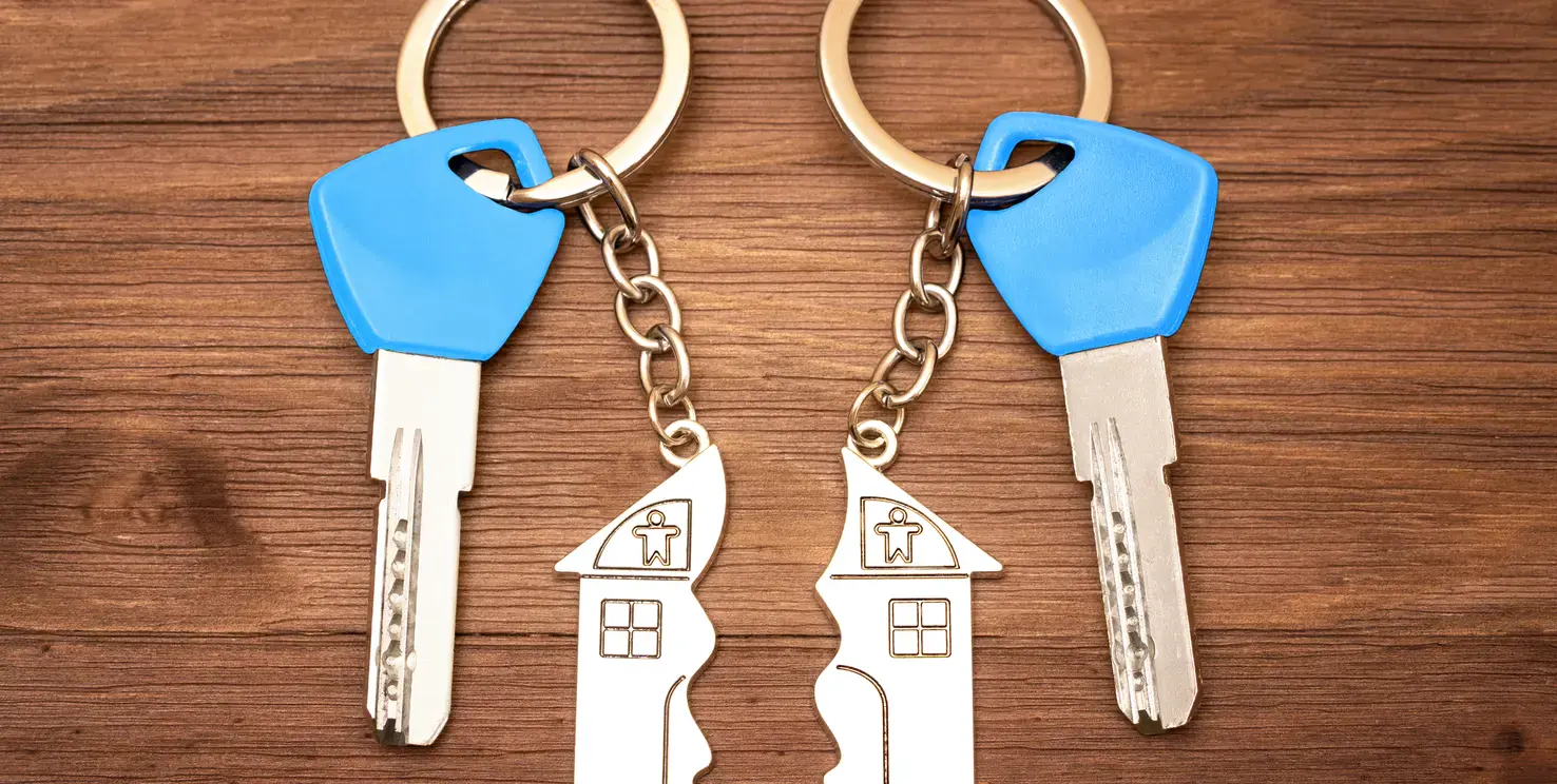 Two house keychains split apart beside two keys, representing selling a house during a divorce