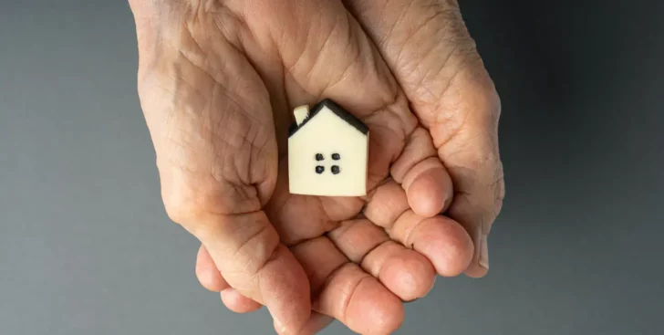 Hands holding a small house model, representing selling an inherited property