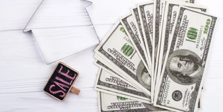 House outline beside cash and a sale sign, representing selling a house for cash