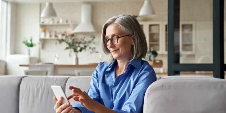 Woman sitting on a couch using her phone to contact a Realtor