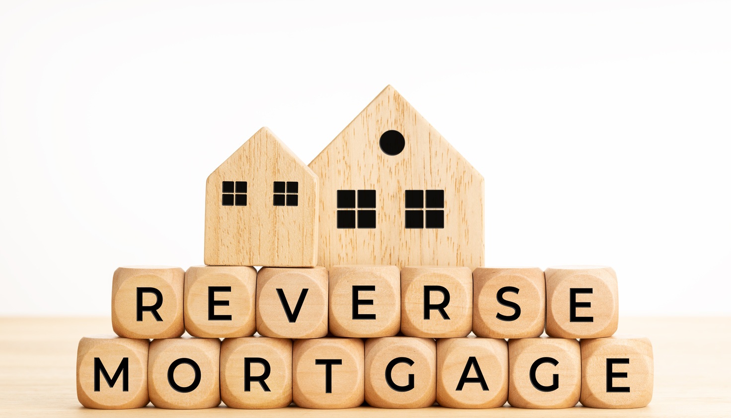 Wooden blocks spelling 'reverse mortgage' with two wooden houses on top, symbolizing selling a house with a reverse mortgage.