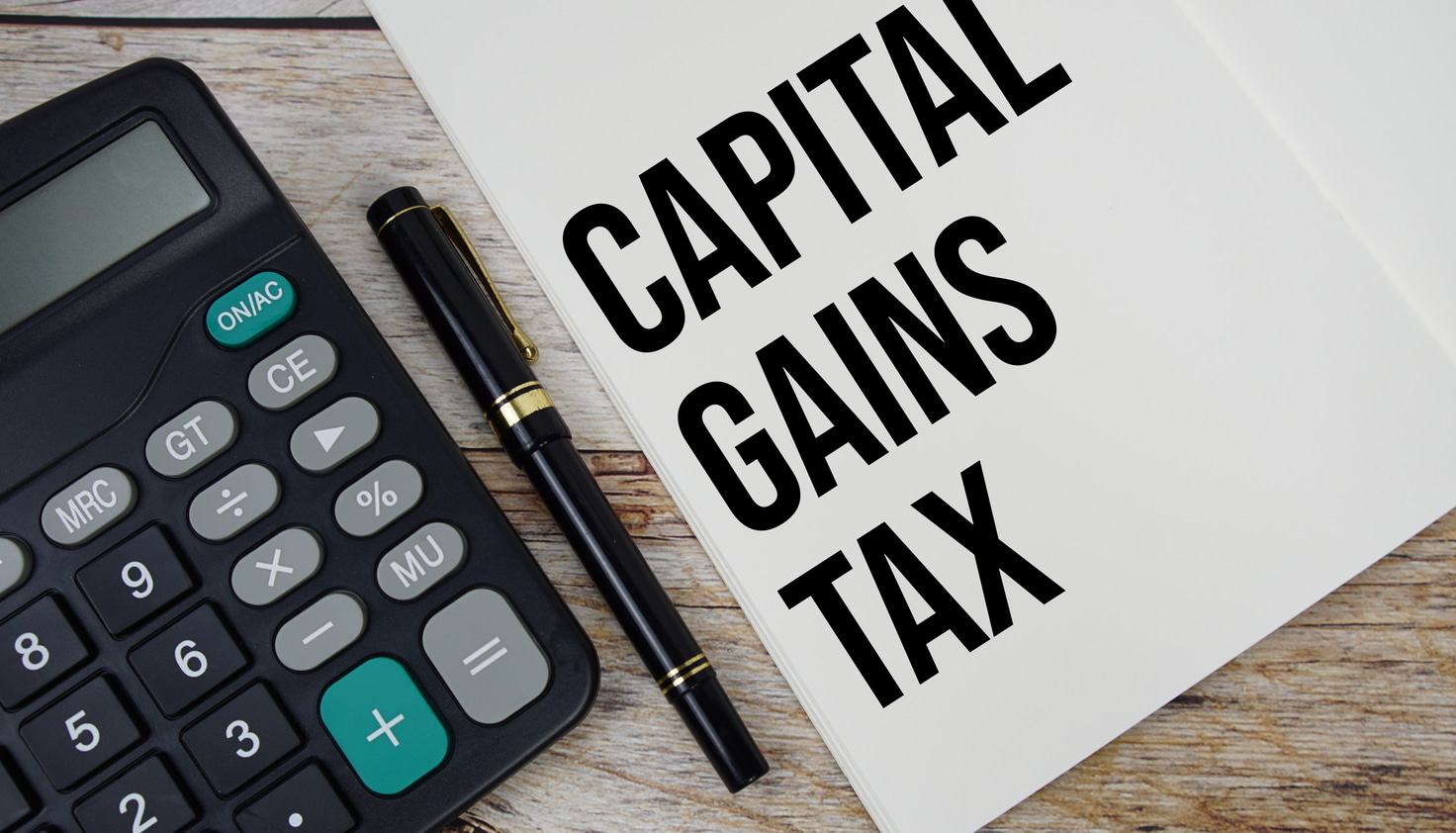 Calculator and folder labeled 'Capital Gains Tax' on a table, symbolizing the calculation of capital gains taxes on a rental property.