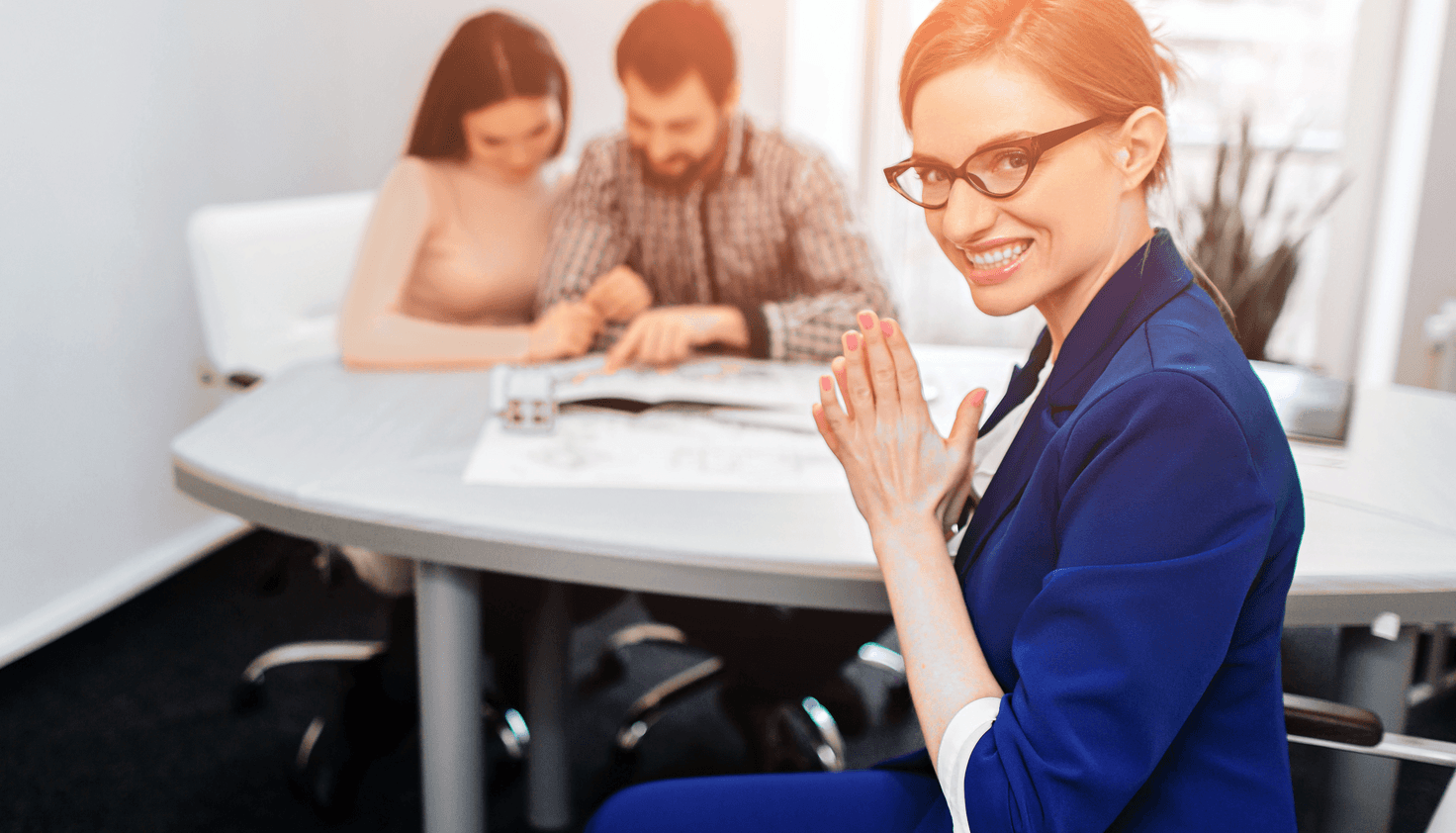 Smug real estate agent clasping hands while unsuspecting clients review documents.