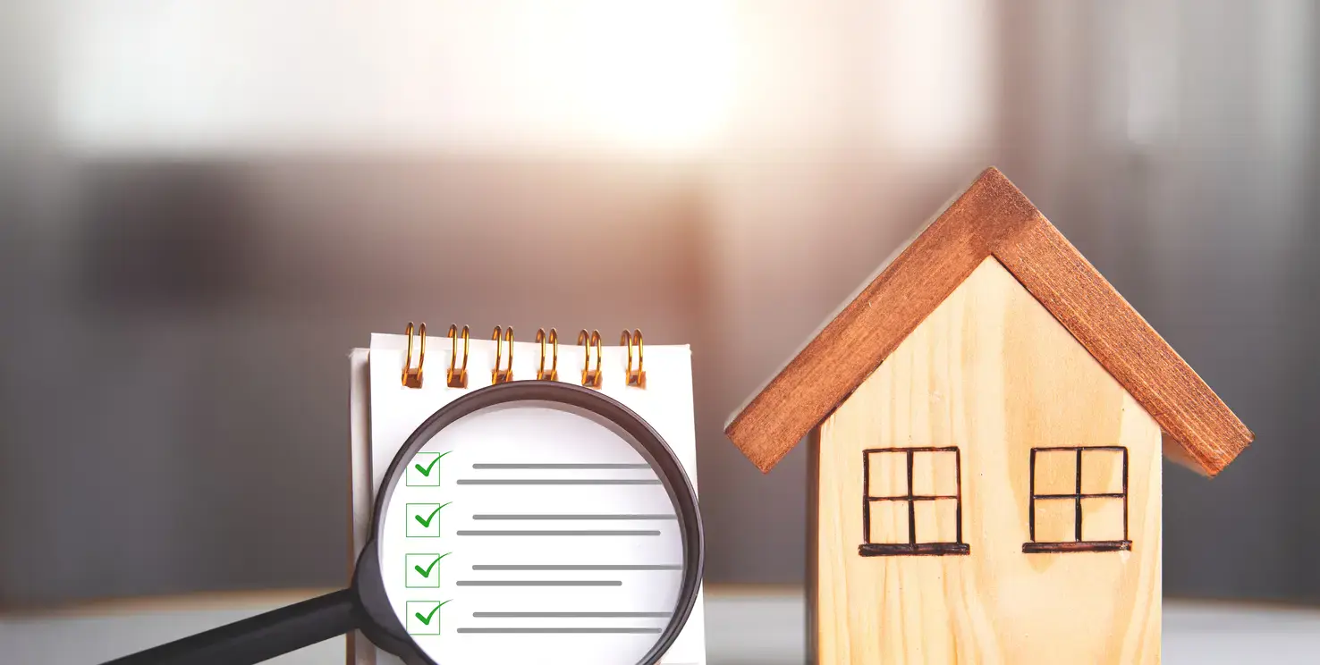 Magnifying glass over a home inspection checklist beside a house model